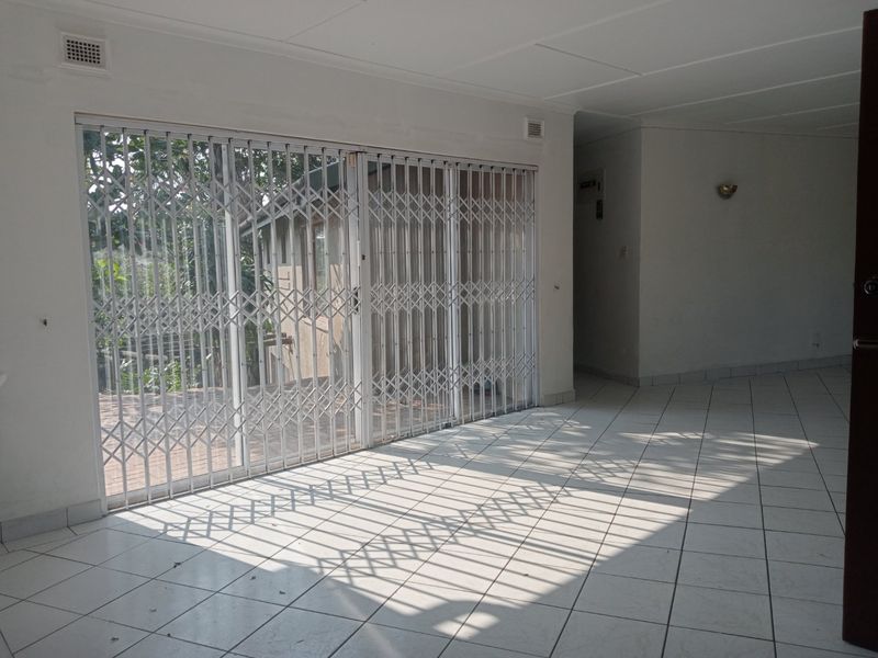 An empty living area featuring white ceramic floor tiles, a wall sconce, and sliding glass doors secured with a metal security gate.
