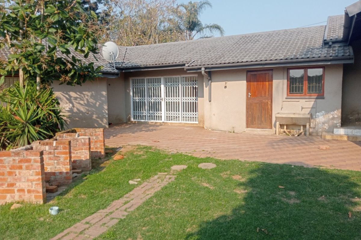 Rear exterior view of the house featuring a paved patio area, security gate, and an outdoor utility sink against a brick wall.