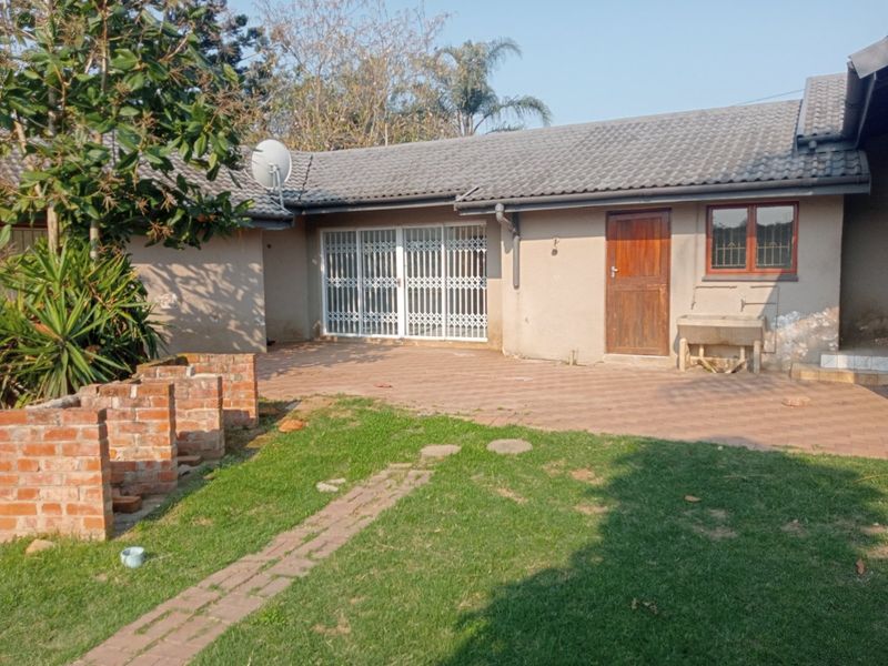 Rear exterior view of the house featuring a paved patio area, security gate, and an outdoor utility sink against a brick wall.