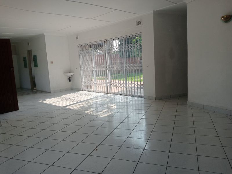 Spacious, empty living area featuring white ceramic floor tiles, a wall-mounted basin, and a security gate leading to the outdoor area.