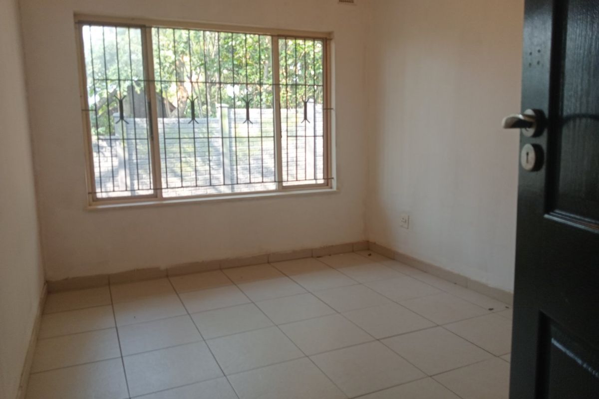 A vacant bedroom featuring neutral tiled flooring and a window fitted with security bars.