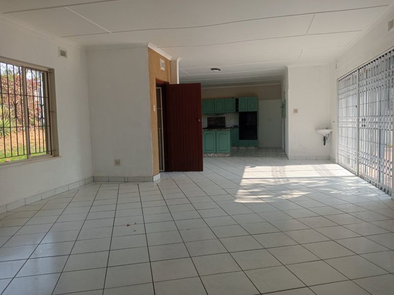 Spacious open-plan living area featuring tiled flooring, security fixtures, and a functional kitchen with built-in cabinetry and oven.