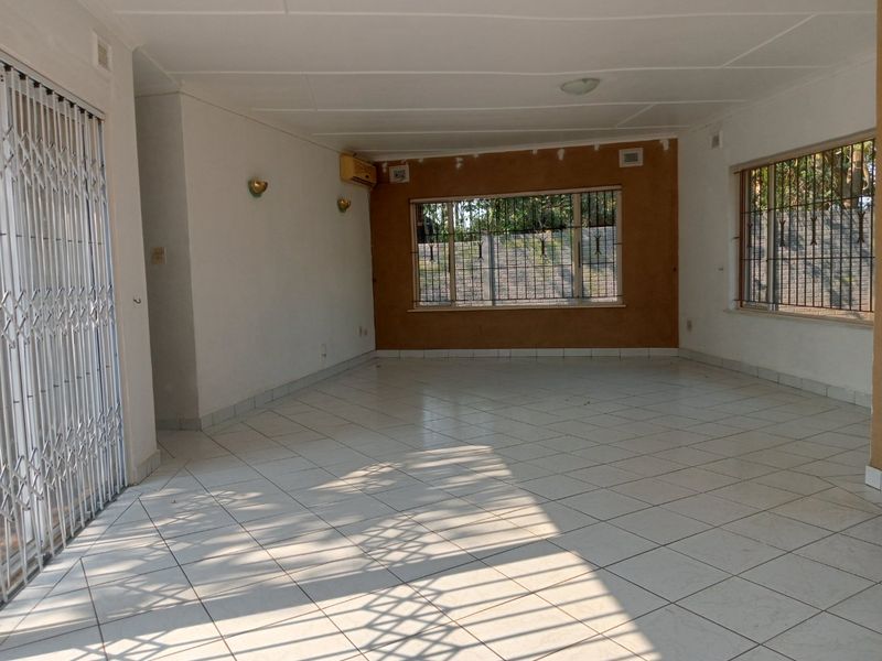 Spacious, empty living area featuring tiled floors, security gates, and wall-mounted air conditioning, currently requiring cosmetic updates to the wall finishes.