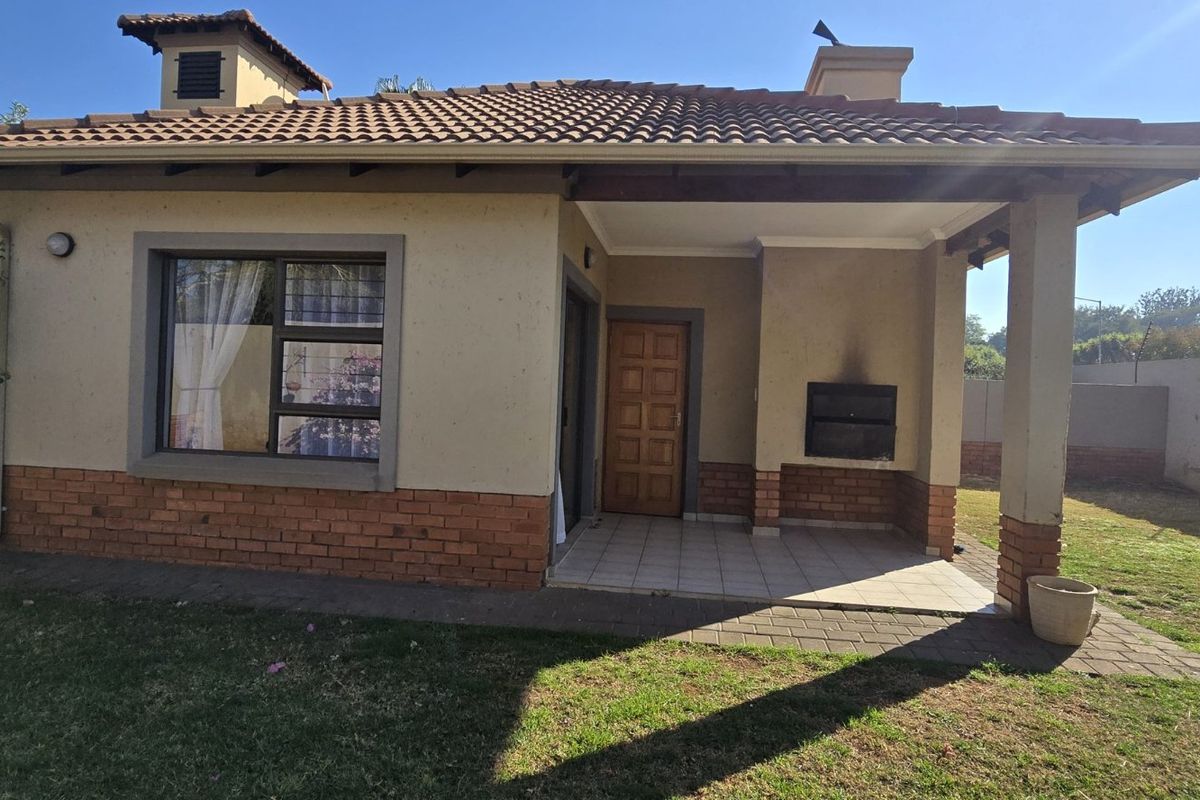 Rear view of the townhouse featuring a covered patio with a built-in braai, brick and plaster facade, and a private garden area.