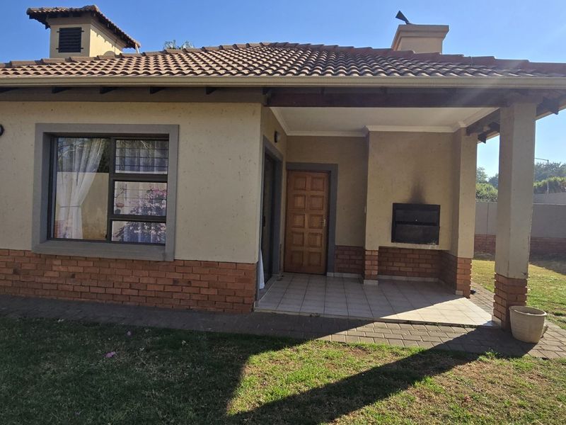 Rear view of the townhouse featuring a covered patio with a built-in braai, brick and plaster facade, and a private garden area.
