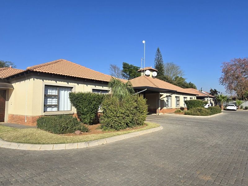 Front exterior view of a townhouse complex featuring a paved driveway, tiled roof, and well-maintained landscaped garden areas.