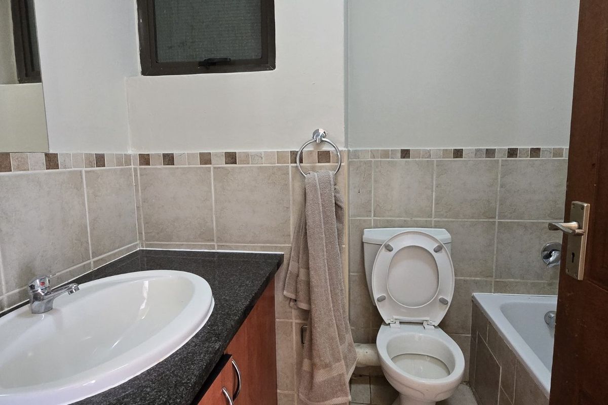A functional bathroom featuring a granite-topped vanity, drop-in basin, toilet, and bathtub with neutral wall tiling.