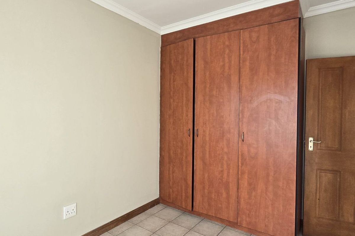 A vacant bedroom featuring tiled flooring, neutral walls, and built-in wooden cupboards with a matching wooden door.