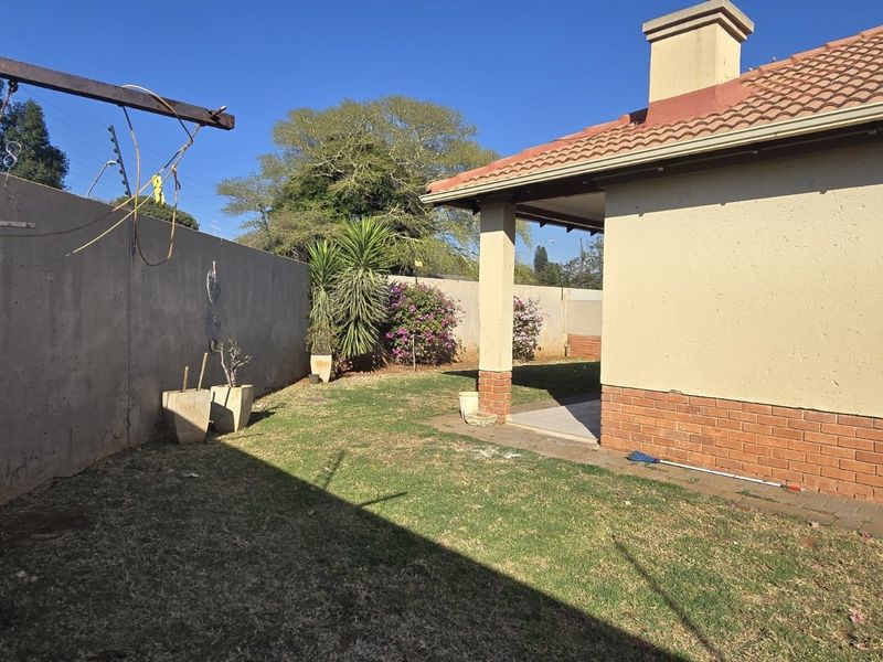 A rear garden view of the townhouse featuring a covered patio, brick plinth detailing, a tiled roof, and a secure boundary wall with electric fencing.