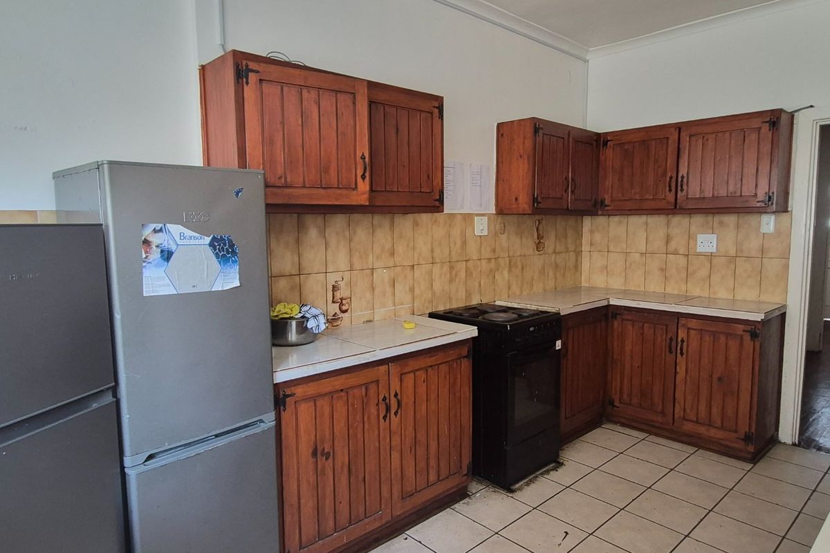 A dated kitchen featuring wooden cabinetry, tiled backsplash, and tiled flooring, offering a functional layout ready for modernization.