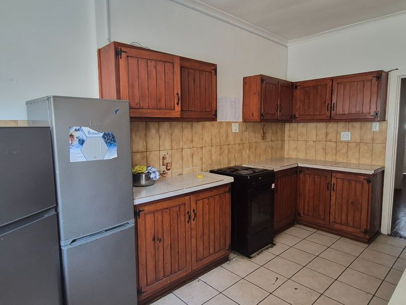 A dated kitchen featuring wooden cabinetry, tiled backsplash, and tiled flooring, offering a functional layout ready for modernization.