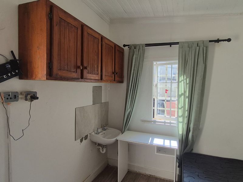 A functional utility or scullery area featuring wall-mounted wooden cabinetry, a small basin, and security bars on the window.