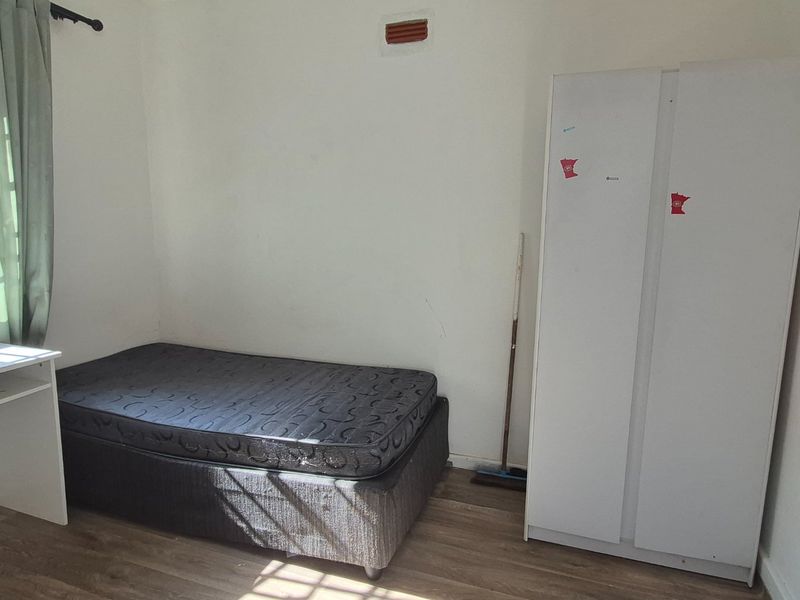 A simple bedroom featuring laminate flooring and a wall-mounted ventilation brick, offering a functional space ready for personalization.