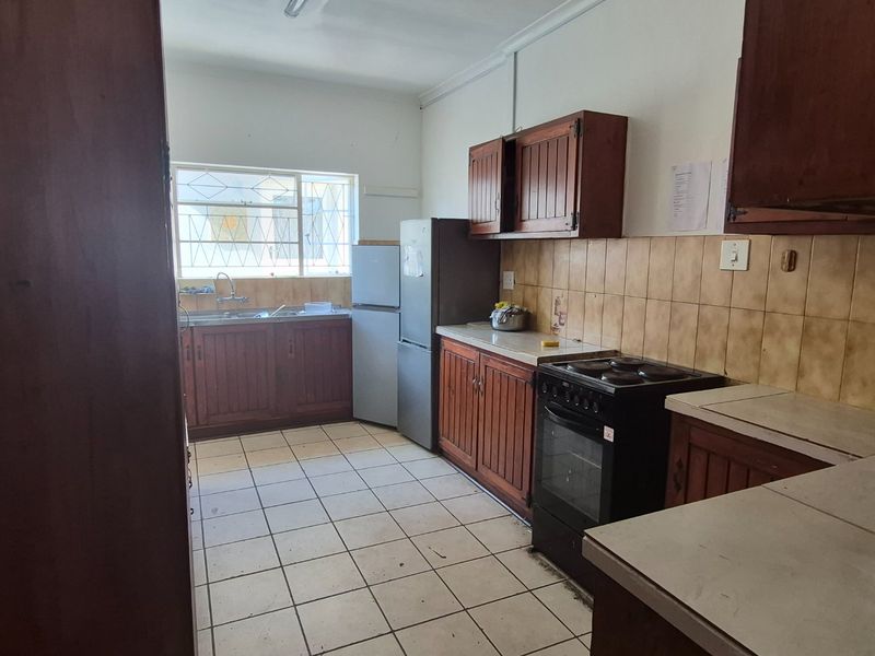 A functional kitchen featuring wooden cabinetry, tiled backsplash, ceramic flooring, and a freestanding stove, offering potential for modernization and aesthetic updates.