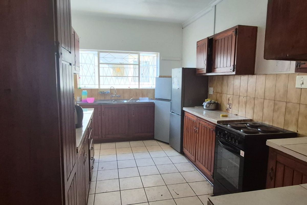 A functional kitchen featuring wooden cabinetry, tiled backsplash, and tiled flooring, offering a dated aesthetic with potential for modernization.