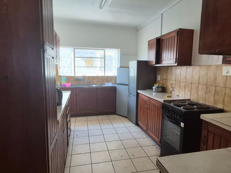 A functional kitchen featuring wooden cabinetry, tiled backsplash, and tiled flooring, offering a dated aesthetic with potential for modernization.