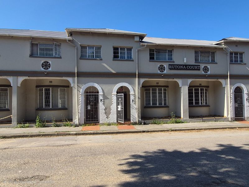 Front elevation of Rutona Court apartment complex featuring arched entrances, security gates, and traditional casement windows with a weathered exterior finish.