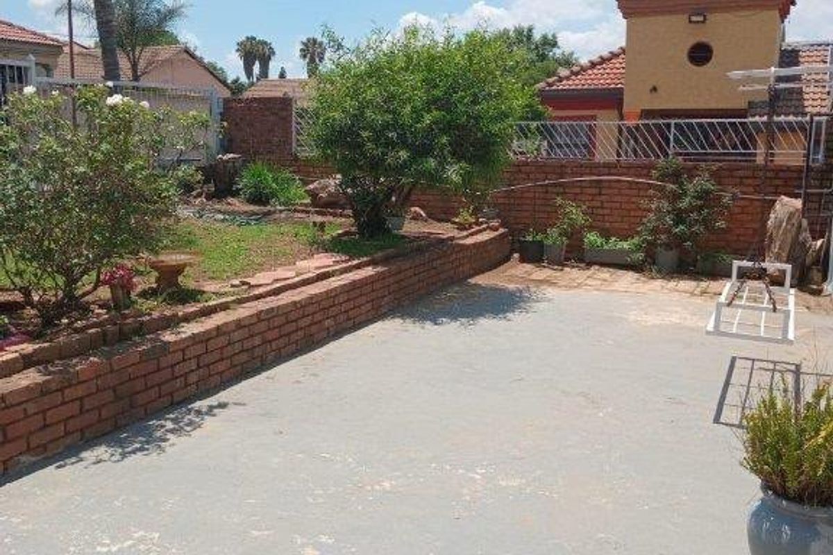 A rear garden area featuring a concrete patio, brick retaining walls, and perimeter fencing, offering a functional outdoor space.