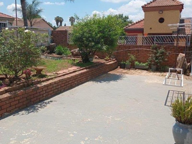 A rear garden area featuring a concrete patio, brick retaining walls, and perimeter fencing, offering a functional outdoor space.