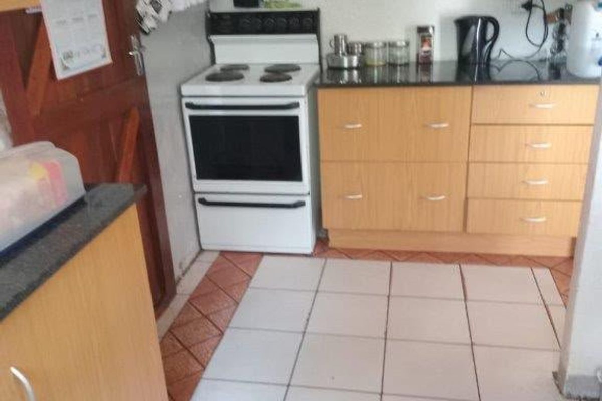 A functional kitchen featuring light wood-tone cabinetry, dark laminate countertops, a freestanding stove, and tiled flooring with a decorative border.