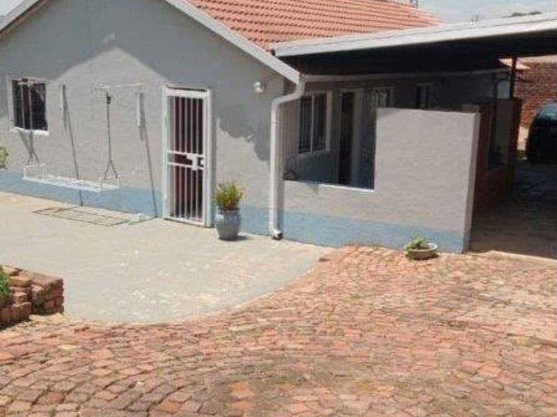 Front view of a single-story house featuring a tiled roof, brick paved driveway, and an attached carport with a concrete patio area.