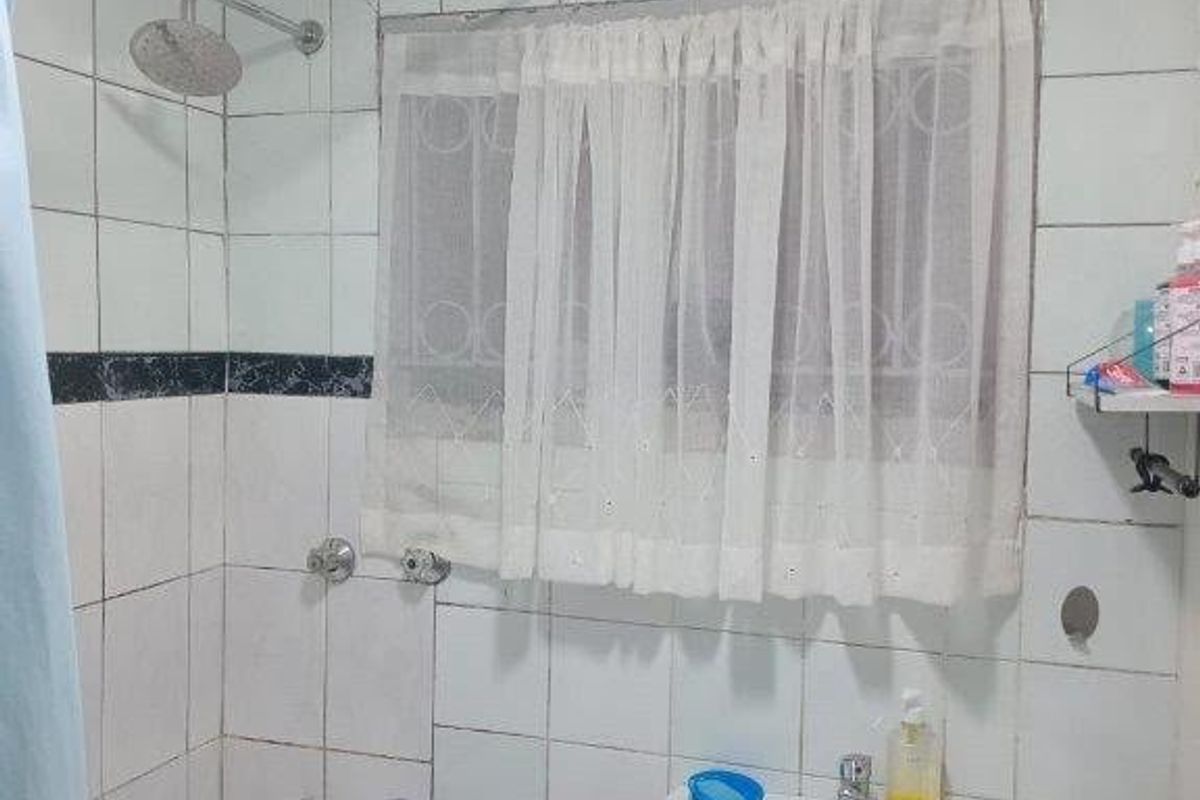 A functional bathroom featuring a pedestal washbasin, bathtub with shower head, and tiled walls. The space would benefit from cosmetic updates and tile repairs.