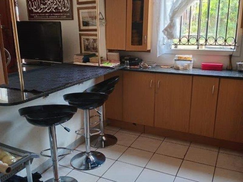 A functional kitchen featuring laminate cabinetry, granite countertops, a breakfast bar, and tiled flooring with security bars on the window.
