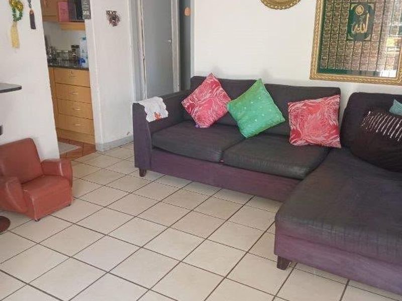 Open plan living area featuring tiled flooring with an adjacent kitchen space visible in the background.