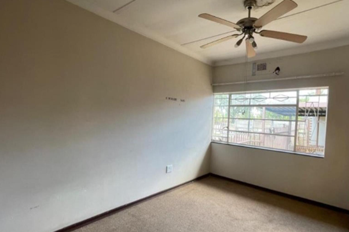 An empty bedroom featuring a ceiling fan, built-in cupboard, and carpeted flooring, with visible signs of ceiling water damage requiring repair.
