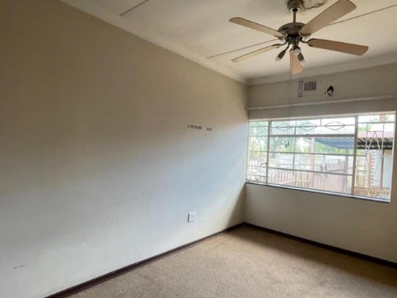 An empty bedroom featuring a ceiling fan, built-in cupboard, and carpeted flooring, with visible signs of ceiling water damage requiring repair.