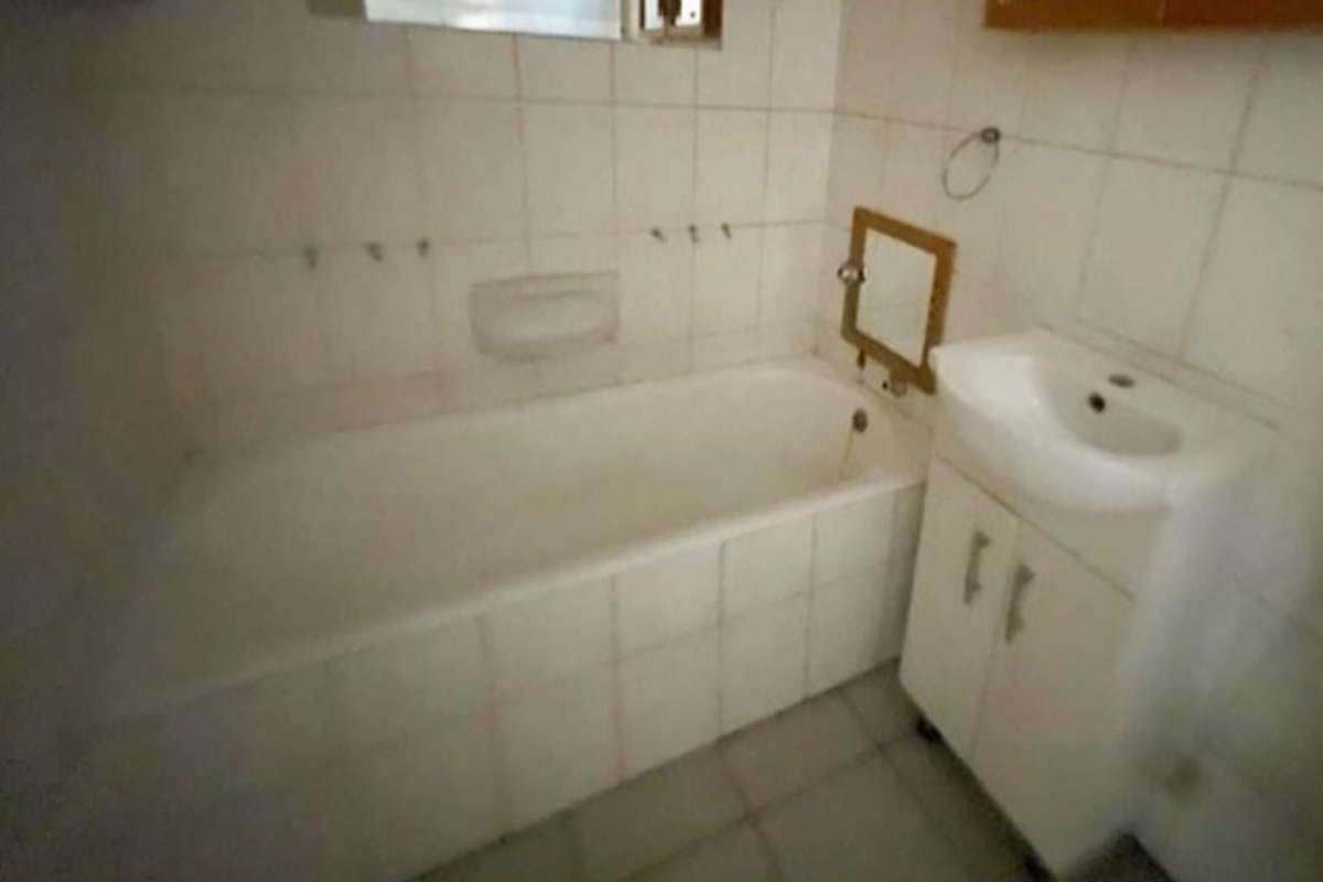A dated bathroom featuring a built-in bathtub, tiled walls, and a vanity cabinet. The space requires cosmetic updates to improve its overall condition.