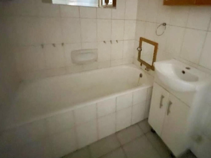 A dated bathroom featuring a built-in bathtub, tiled walls, and a vanity cabinet. The space requires cosmetic updates to improve its overall condition.