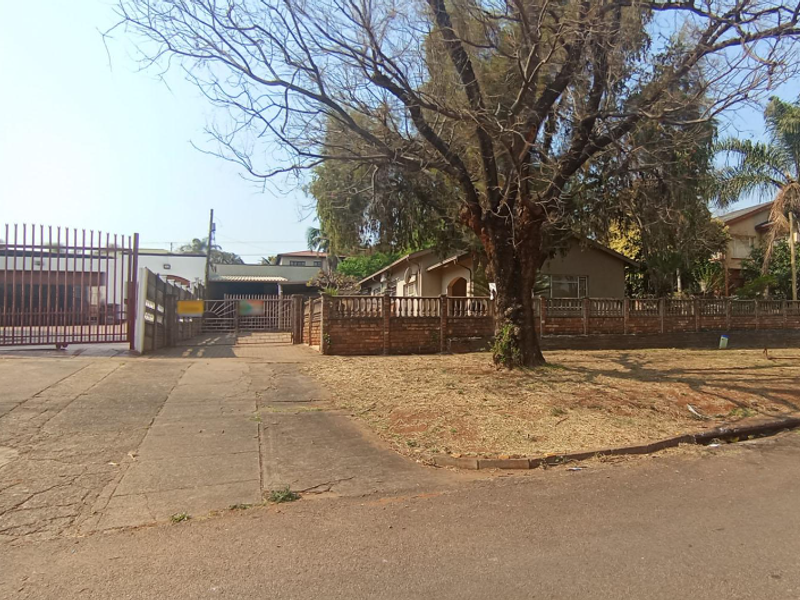 Front view of the property featuring a concrete driveway, metal security gate, and a brick boundary wall with mature trees.