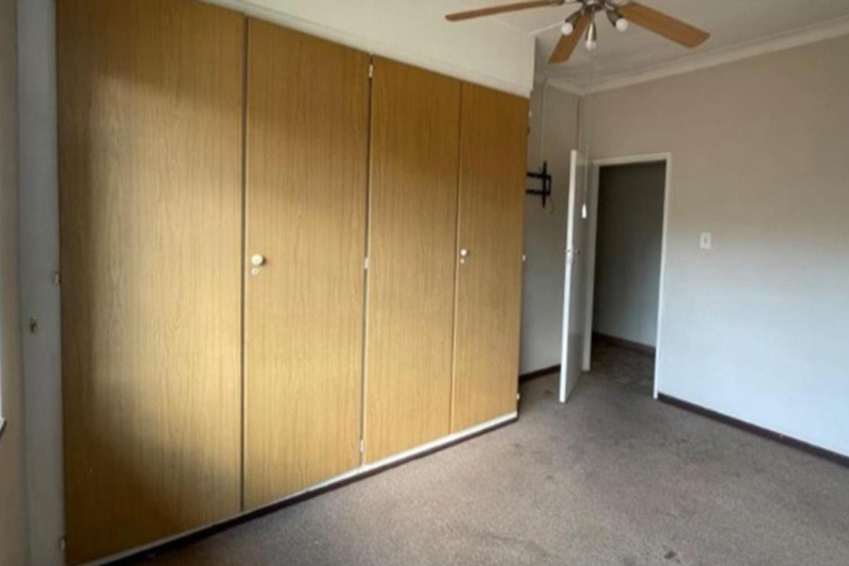 A spacious bedroom featuring extensive built-in wooden cupboards, a ceiling fan, and neutral wall finishes, offering a blank canvas for personalization.