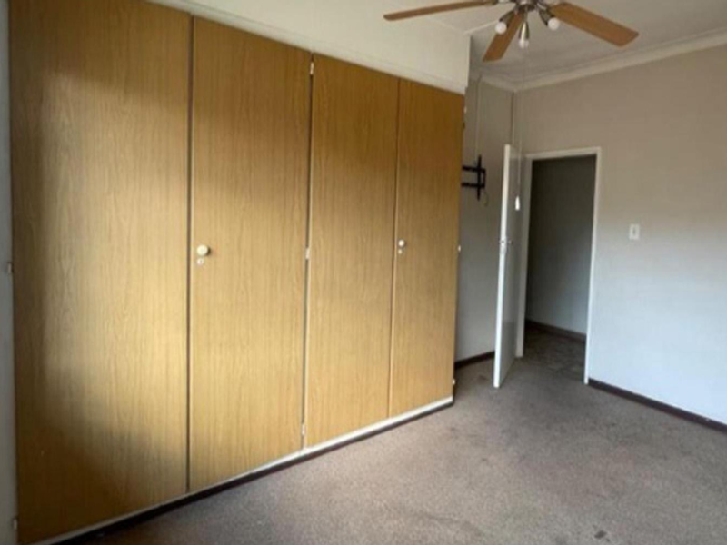 A spacious bedroom featuring extensive built-in wooden cupboards, a ceiling fan, and neutral wall finishes, offering a blank canvas for personalization.