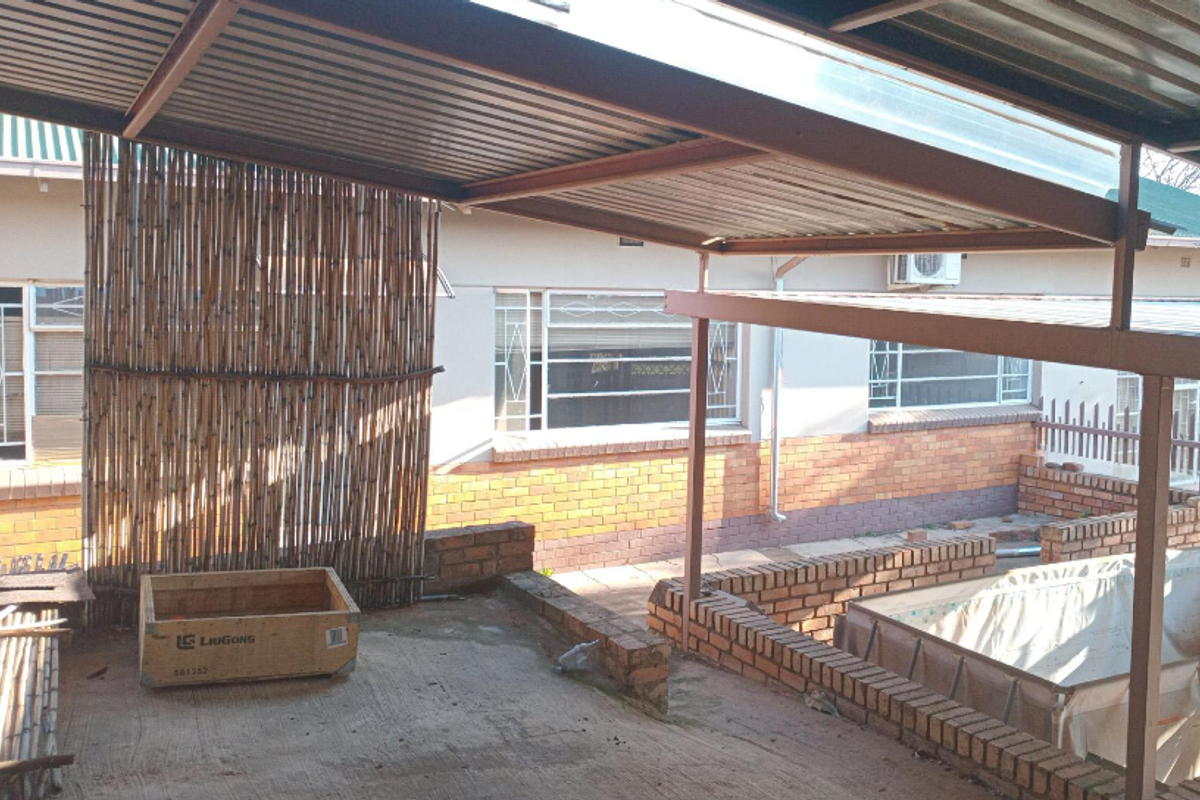 Covered outdoor patio area featuring brick retaining walls, corrugated metal roofing, and steel support structures, providing a functional space for outdoor living.