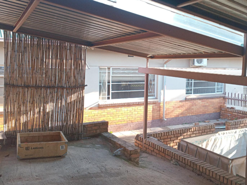Covered outdoor patio area featuring brick retaining walls, corrugated metal roofing, and steel support structures, providing a functional space for outdoor living.