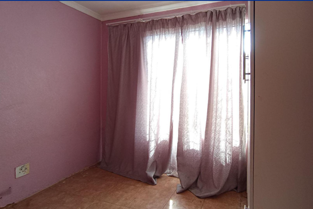 An empty bedroom featuring tiled flooring, built-in cupboard space, and a curtained window, requiring cosmetic updates to the wall finishes.