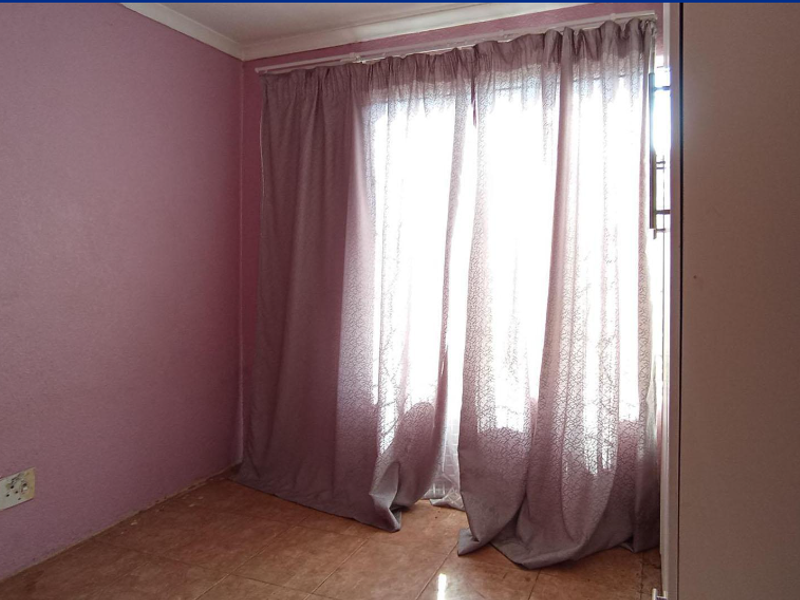An empty bedroom featuring tiled flooring, built-in cupboard space, and a curtained window, requiring cosmetic updates to the wall finishes.