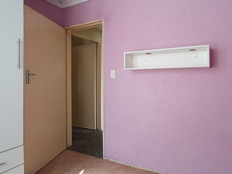 A bedroom featuring a built-in wardrobe and a wall-mounted shelf, finished with pink wall paint and tiled flooring.