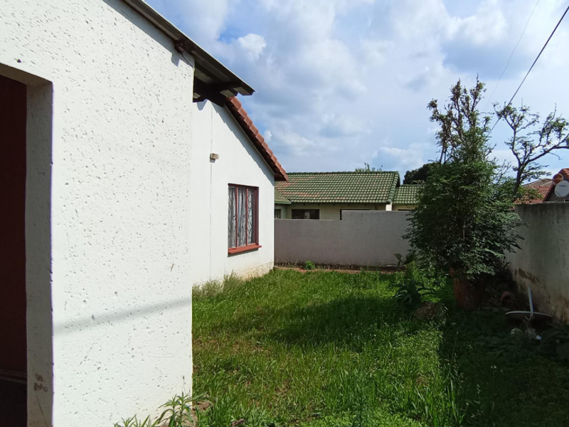 Rear exterior view of the property featuring a small garden area, boundary walls, and tiled roof sections.