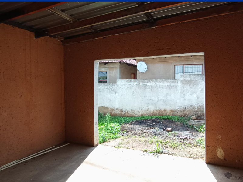 An unfinished garage space with exposed roof structure and textured walls, offering direct access to the rear yard area.