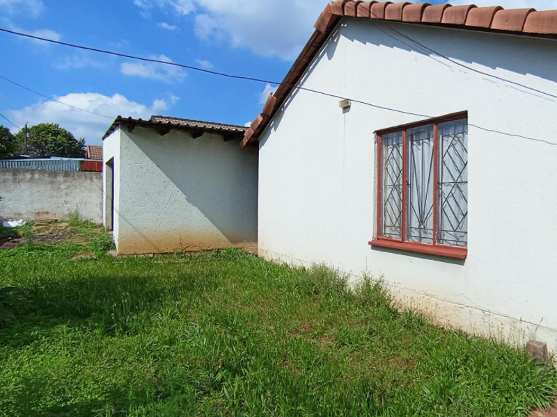 Rear view of the property showing the exterior wall, security-barred window, and a small backyard area with overgrown grass.