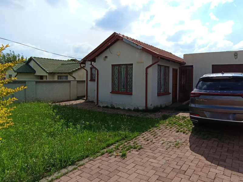 Front view of a single-story house featuring a tiled roof, paved driveway, and attached garage, set within a residential property with a lawn.