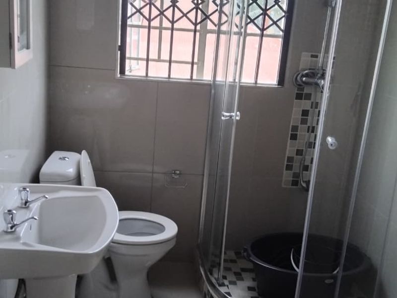 A functional bathroom featuring a pedestal basin, toilet, and a corner shower enclosure with tiled walls and security bars on the window.