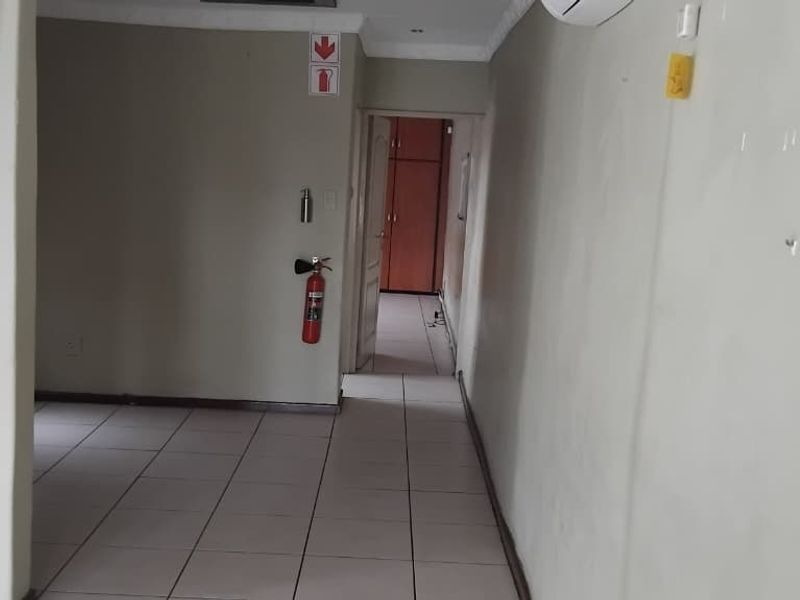 A functional hallway featuring tiled flooring, wall-mounted air conditioning, and a fire safety installation, leading towards an adjacent room.