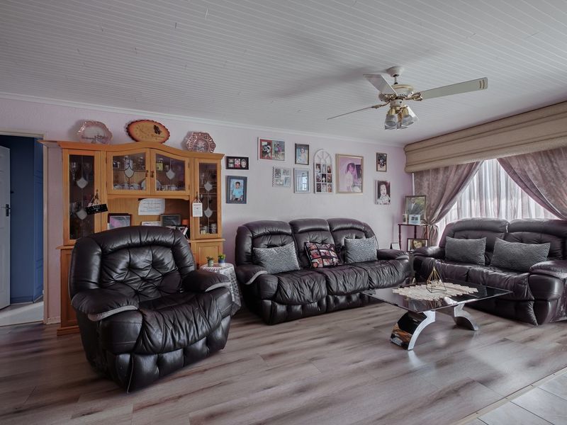 A comfortable living room featuring laminate flooring, a tongue and groove ceiling, and a central ceiling fan.