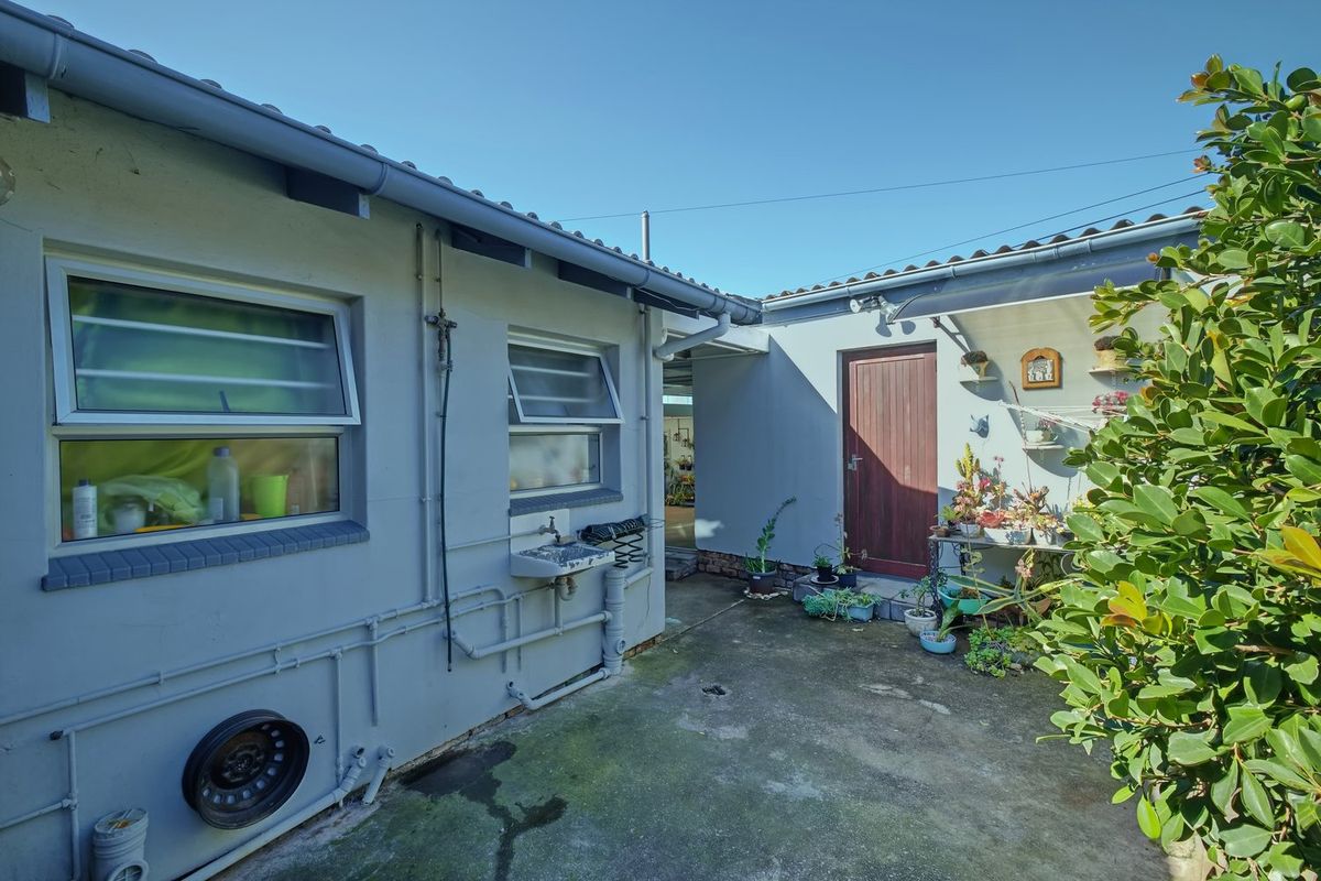 A functional rear courtyard area featuring a concrete surface, external utility sink, and access to the main dwelling via a wooden door.