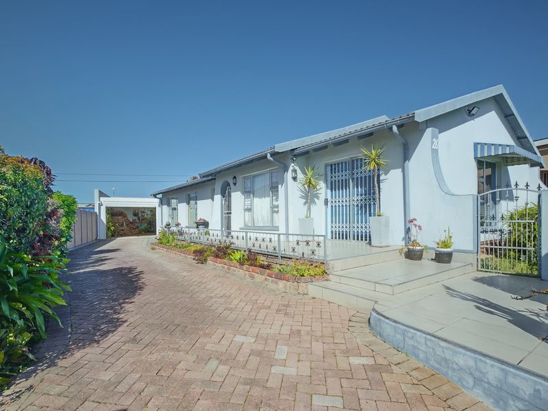 Front elevation of a single-story house featuring a paved driveway, tiled porch, security gates, and a detached carport.