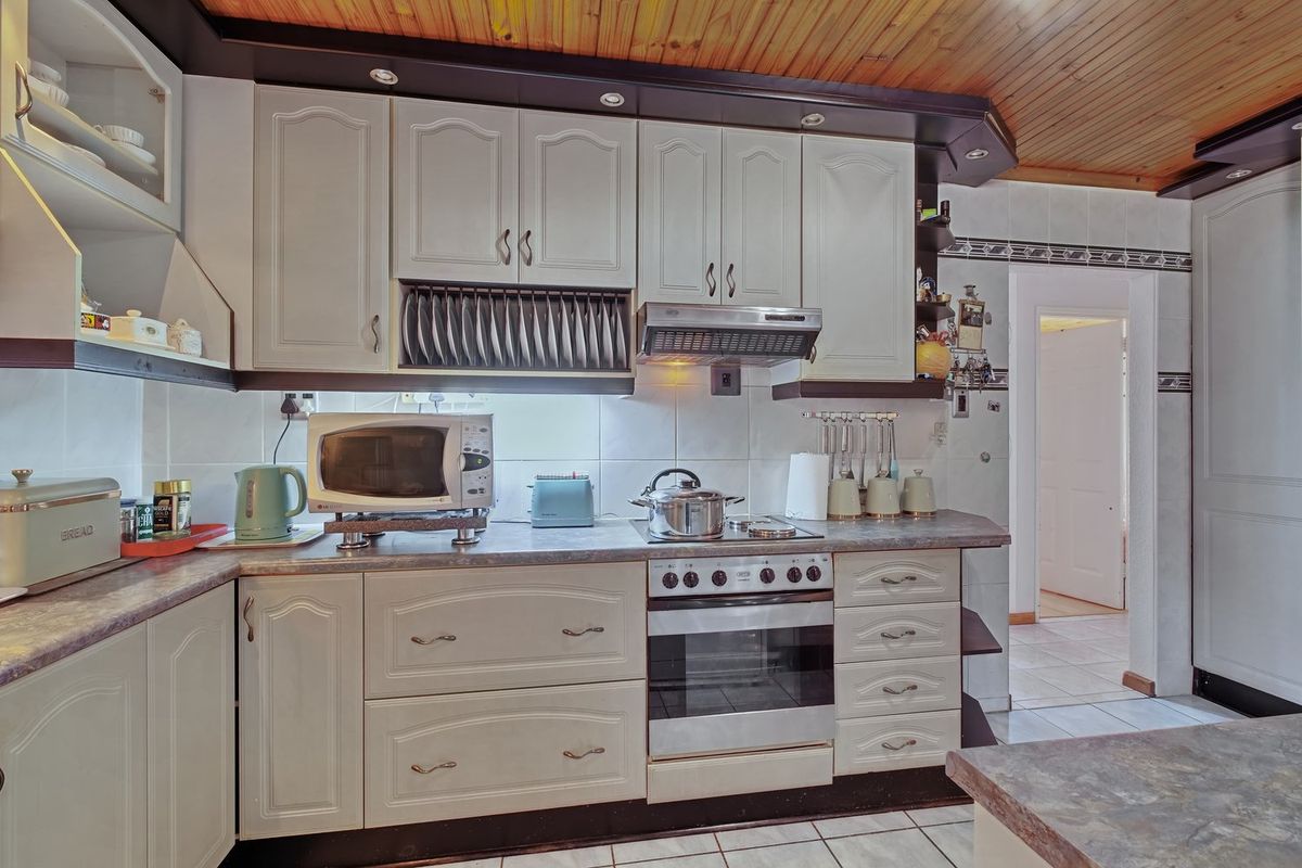 A functional kitchen featuring light-toned cabinetry, laminate countertops, a built-in oven with extractor fan, and a distinctive timber-paneled ceiling.